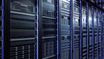 Row of black server racks with blue LED lights in a modern data centre, filled with storage drives and network hardware.